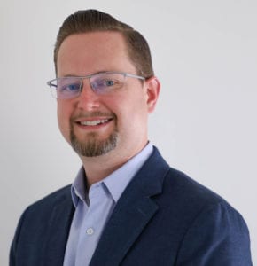 A man in glasses and a suit smiling for the camera.